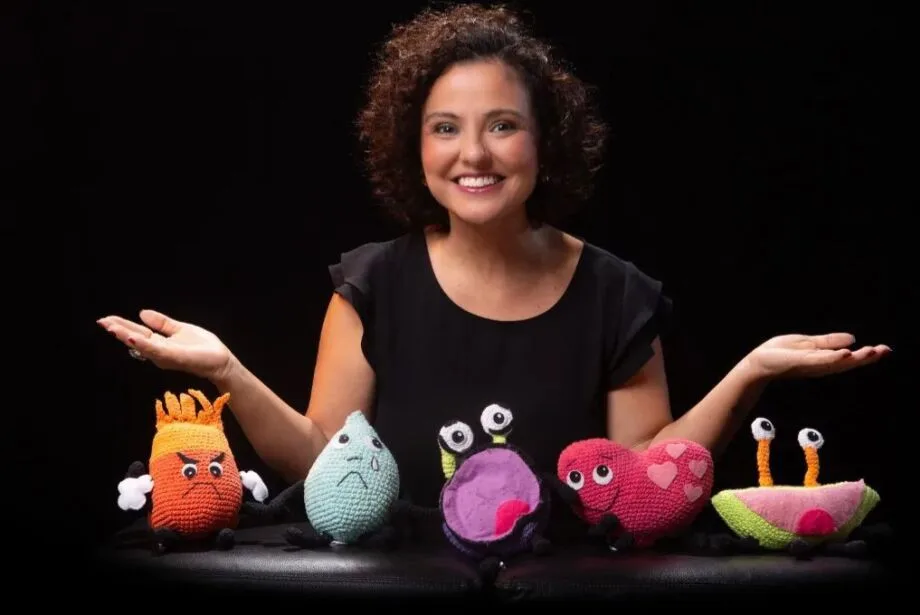 Autora Fernanda Cortês em frente a bichinhos de pelúcia que representam as emoções.